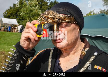 Henrichenburg, Waltrop, Germania. 12 agosto 2023. Un fan dello steampunk cerca di scattare foto con i suoi occhiali monoclici. Gli appassionati di steampunk, i gruppi in costumi e i visitatori, molti in abiti retrò-futuristici o di ispirazione vittoriana, si divertono nonostante le forti docce a pioggia del primo giorno del weekend del Festival del Giubileo di Steampunk presso lo storico skilift di Henrichenburg, un monumento architettonico e sito del patrimonio industriale. Crediti: Imageplotter/Alamy Live News Foto Stock