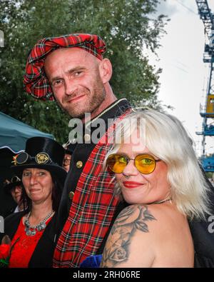 Henrichenburg, Waltrop, Germania. 12 agosto 2023. Un paio di abiti Steampunk ispirarono le Highland scozzesi. Gli appassionati di steampunk, i gruppi in costumi e i visitatori, molti in abiti retrò-futuristici o di ispirazione vittoriana, si divertono nonostante le forti docce a pioggia del primo giorno del weekend del Festival del Giubileo di Steampunk presso lo storico skilift di Henrichenburg, un monumento architettonico e sito del patrimonio industriale. Crediti: Imageplotter/Alamy Live News Foto Stock