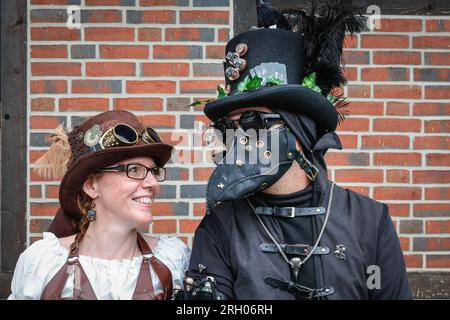 Henrichenburg, Waltrop, Germania. 12 agosto 2023. Darksteam il Dottore Pest posa con il suo compagno. Gli appassionati di steampunk, i gruppi in costumi e i visitatori, molti in abiti retrò-futuristici o di ispirazione vittoriana, si divertono nonostante le forti docce a pioggia del primo giorno del weekend del Festival del Giubileo di Steampunk presso lo storico skilift di Henrichenburg, un monumento architettonico e sito del patrimonio industriale. Crediti: Imageplotter/Alamy Live News Foto Stock