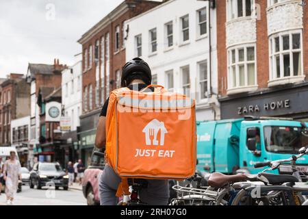 Un autista che consegna Just Eat seduto sulla sua bicicletta con un grande contenitore arancione Just Eat che riposa sulla schiena. Richmond, Surrey Foto Stock