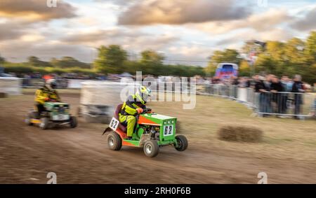 Due piloti di rasaerba da corsa si lanciano al crepuscolo con la BLMRA 500, una corsa notturna di 500 km in stile le Mans in un campo nel West Sussex, Regno Unito. La British Lawn Mower Racing Association organizza il suo 50° anniversario di 12 ore di gara durante la notte sabato/domenica con 52 squadre, ognuna con tre piloti. Foto Stock