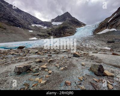 Oteren, Contea di Troms, Norvegia. 12 agosto 2023. Vista dall'escursione attraverso la valle del fiume glaciale da e verso la cima del ghiacciaio Steindal (Steindalsbreen) deflusso nella Norvegia artica. Lo Steindal Glacier è una destinazione popolare per gli escursionisti ambiziosi, nonché per coloro che vogliono assistere a un'incredibile riduzione. I cartelli eretti lungo la strada raccontano dove un tempo era il ghiaccio e negli ultimi anni, il deflusso ha perso molti metri di lunghezza e altezza. La regione di Tromso dovrebbe anche rompere ufficialmente le ''temperature più alte registrate'' il 12 agosto in caso di oltre 20c. (Immagine di credito: © sa Foto Stock