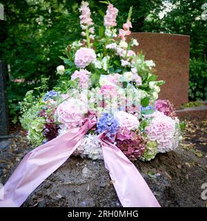 una corona di ortensie rosa, bianca e blu con un arco rosa in lutto su una tomba dopo un funerale Foto Stock