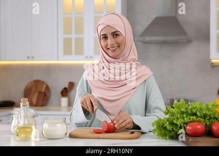 Donna musulmana che prepara una deliziosa insalata con verdure al tavolo bianco in cucina Foto Stock