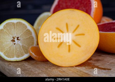 diversi tipi di agrumi in tavola, pompelmo rosso, mandarini arancioni e limone giallo e cachi in tavola Foto Stock