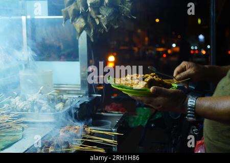 La scena di Sate Padang, un tipo di piatto indonesiano a base di carne spiedata e grigliata, cucinato a fiamma aperta in una bancarella di cibo di strada. Foto Stock
