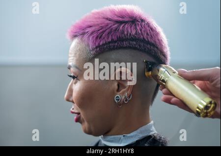 Il parrucchiere rasa il tempio di una cliente femminile. Donna asiatica con capelli corti rosa in barbiere. Foto Stock