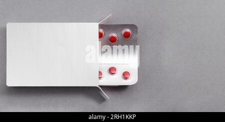 Confezione con compresse rosse farmaci mock-up, modello su tavolo grigio. Pillole antibiotiche in blister. Foto Stock