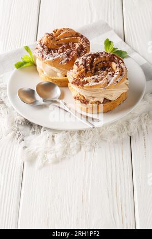 Dessert francese paris-brest con zucchero a velo e primo piano di cacao su un piatto sul tavolo di legno. Verticale Foto Stock