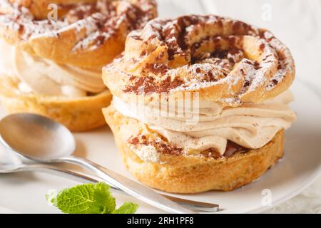 Classica torta francese Paris Brest di pasta choux con panna decorata con zucchero a velo e cacao da vicino in un piatto sul tavolo. Orizzontale Foto Stock