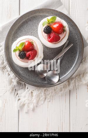 Fragole, mirtilli, lamponi e crema decorano le torte Anna Pavlova su un piatto sul tavolo di legno. Vista dall'alto verticale Foto Stock