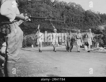 Campagna della Malesia, dicembre 1941 – febbraio 1942. Una sentinella giapponese osserva l'inviato britannico di resa guidato dal tenente generale Arthur Percival (all'estrema destra) scortato dal tenente colonnello Sugita Ichiji (al centro) in rotta per i negoziati di resa con la venticinquesima armata imperiale giapponese, Singapore, il 15 febbraio 1942. Foto Stock