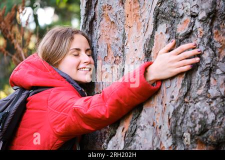 Escursionista sorridente che abbraccia un albero nella foresta. Foto Stock