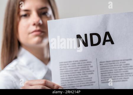La donna in bianco tiene la NDA, avvertimento di linguaggio limitato. Concentrarsi sull'accordo di non divulgazione. Devi firmare o aver firmato; le parole sono limitate Foto Stock