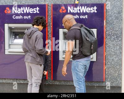 Due uomini che usano un distributore di contanti presso la filiale NatWest di Hammersmith, Londra, Regno Unito Foto Stock