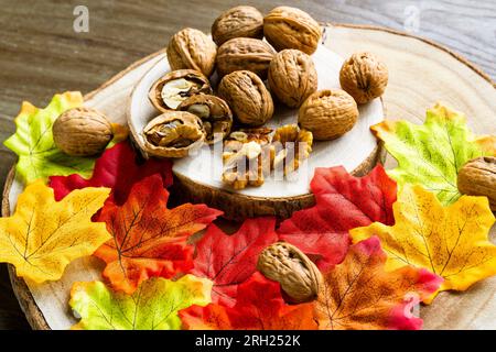 Gruppo di noci su un vassoio di legno naturale e alcune colorate foglie autunnali Foto Stock