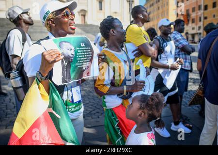 Roma, Roma, Italia. 12 agosto 2023. Una ragazza senegalese legge le parole di Ousmane Sonko da un cartello mentre sua madre grida slogan di protesta durante la manifestazione organizzata dal partito italiano Pastef a Roma per il rilascio di Ousmane Sonko. Ousmane Sonko, leader del partito di opposizione senegalese Pastef (Patriotes africains du Sénégal pour le travail, l'éthique et la fraternité) fu arrestato all'inizio di agosto 2023 con l'accusa di incitamento all'insurrezione. È stato uno dei candidati favoriti alle elezioni senegalesi del febbraio 2024. (Immagine di credito: © Marcello Valeri/ZUMA Press Wire) USO EDITORIALE ONL Foto Stock