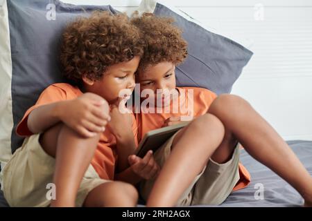 Fratelli seduti sul letto dei genitori e guardando cartoni animati su un tablet Foto Stock