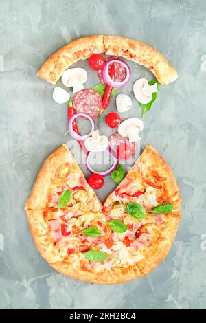 Pizza fresca con un pezzo tagliato su sfondo grigio. Ingredienti per la pizza. Foto Stock