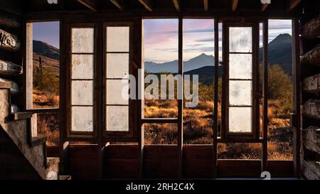 Paesaggio del deserto del vecchio ovest visto attraverso il muro danneggiato di una vecchia foto composita di una cabina Foto Stock