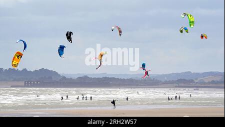 Gli amanti del kite surf apprezzano il clima ventoso di Camber Sands, nell'East Sussex. Secondo il Met Office, le temperature potrebbero raggiungere i 30 °C in alcune parti del Regno Unito la prossima settimana, dopo che le forti piogge bagnano il paese. Data foto: Domenica 13 agosto 2023. Foto Stock