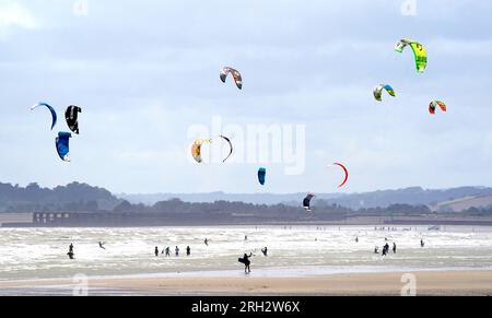 Gli amanti del kite surf apprezzano il clima ventoso di Camber Sands, nell'East Sussex. Secondo il Met Office, le temperature potrebbero raggiungere i 30 °C in alcune parti del Regno Unito la prossima settimana, dopo che le forti piogge bagnano il paese. Data foto: Domenica 13 agosto 2023. Foto Stock