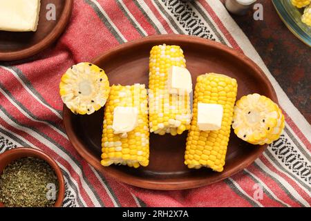 Piatto di pannocchie di mais bollite con burro su sfondo scuro Foto Stock