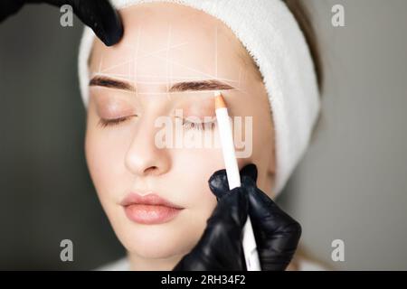 Cosmetologo Mappatura sopracciglia di donna con matita bianca prima del trattamento di trucco permanente Foto Stock