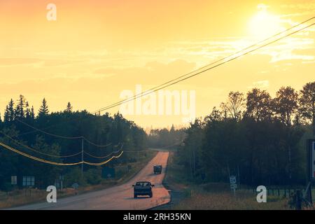 Le auto viaggiano lungo un'autostrada canadese mentre il sole proietta un bagliore giallo nel cielo Foto Stock