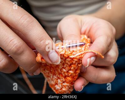 Mani che tengono un uncinetto lavorando su un pezzo d'arte di colore zucca (arancione) Foto Stock