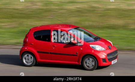 Milton Keynes, Regno Unito - 11 agosto 2023: Red 2011 peugeot 107 che guida su una strada di campagna inglese. Foto Stock