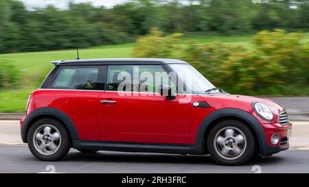 Milton Keynes, Regno Unito - 13 agosto 2023: 2010 Mini car rossa che guida su una strada di campagna inglese. Foto Stock