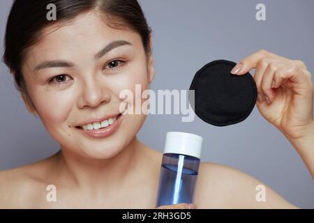 Ritratto di una donna asiatica moderna con un makeup Remover e un tampone di cotone nero su sfondo blu. Foto Stock