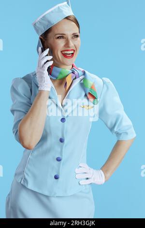 sorridente ed elegante assistente di volo su sfondo blu in uniforme blu che parla su uno smartphone. Foto Stock