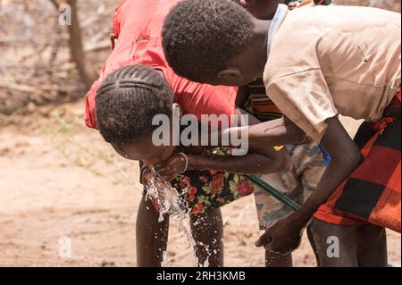 Giovani bambini kenioti che a turno bevono da una pipa d'acqua dolce con acqua proveniente dal vicino foro, contea di Baringo, Kenya Foto Stock