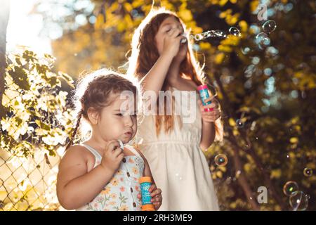 Due bambine, sorelle all'aperto in abiti bianchi, che fanno babble di sapone Foto Stock