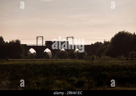Sillhouette di una DB Cargo rail UK classe 66 locomotiva (66063) che attraversa il viadotto di Garnock Longford, a sud di Kilwinning, Ayrshire (fiume Garnock) Foto Stock