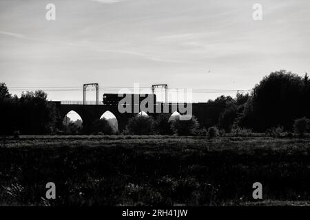 Sillhouette di una DB Cargo rail UK classe 66 locomotiva (66063) che attraversa il viadotto di Garnock Longford, a sud di Kilwinning, Ayrshire (fiume Garnock) Foto Stock