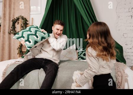 Scontri con i cuscini, giochiamo con un giovane padre felice e una figlia bambina, divertendosi a ridere per i giochi divertenti, scherzando e legando insieme a casa. Papà e gioco emozionati Foto Stock