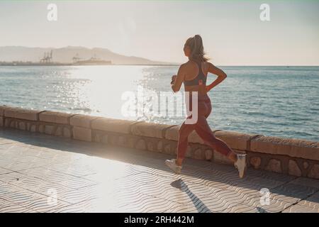 Atletica bella donna che corre attivamente sul lungomare Foto Stock