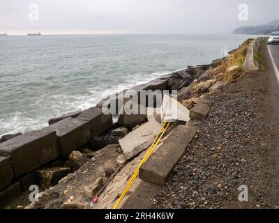 Posto pericoloso. Barriera stradale crollata sul lato di una montagna. Vecchi blocchi di fortificazioni della costa. Strutture in cemento a terra. Protezione aga Foto Stock