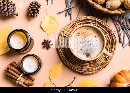 Concetto estetico autunnale. Tazza di caffè a latte con spezie di zucca, candele, zucca e foglie gialle autunnali su sfondo beige. Foto Stock