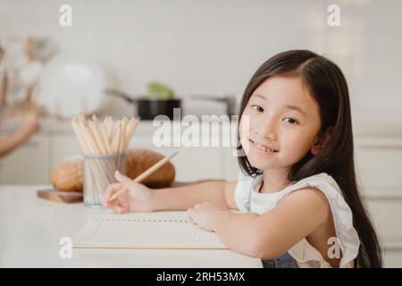 Carina bambina felice di imparare l'educazione facendo il lavoro a casa in vacanza Foto Stock