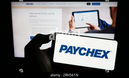 Persona che possiede uno smartphone con il logo della società di outsourcing statunitense Paychex Inc. Sullo schermo di fronte al sito Web. Concentrarsi sul display del telefono. Foto Stock