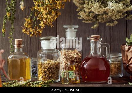 Bottiglie di olio essenziale, erbe e tinture, con essiccazione di St. L'erba di Giovanni, la freccia e l'agromia appesi sullo sfondo Foto Stock