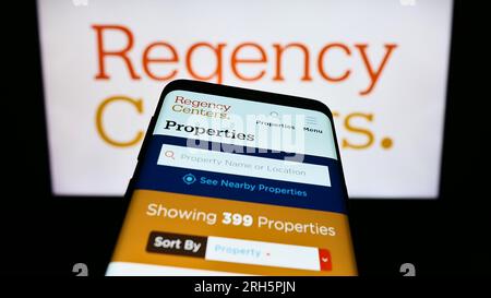 Telefono cellulare con sito Web della società statunitense Regency Centers Corporation sullo schermo davanti al logo aziendale. Mettere a fuoco in alto a sinistra sul display del telefono. Foto Stock
