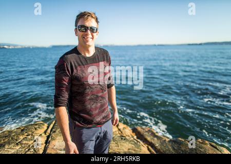 Ritratto di un uomo che si staglia su un affioramento roccioso sulla riva. Foto Stock