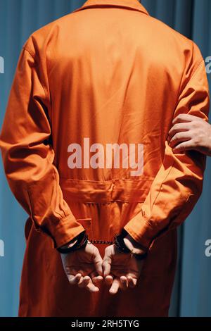 Agente di polizia che cammina arrestato criminale in uniforme arancione fino in prigione, vista dal retro Foto Stock