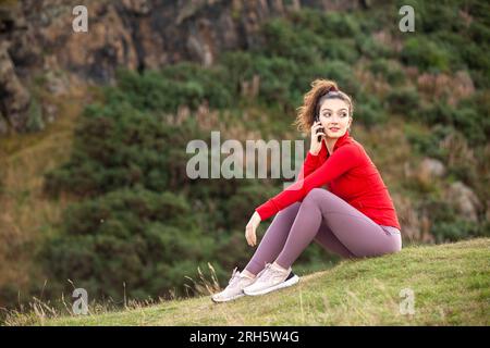 Una giovane donna seduta con i leggings e che parla al telefono Foto Stock