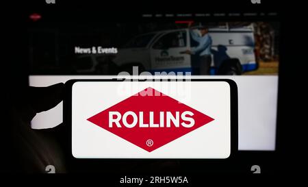Persona che possiede uno smartphone con il logo della società statunitense di disinfestazione Rollins Inc. Sullo schermo di fronte al sito Web. Concentrarsi sul display del telefono. Foto Stock
